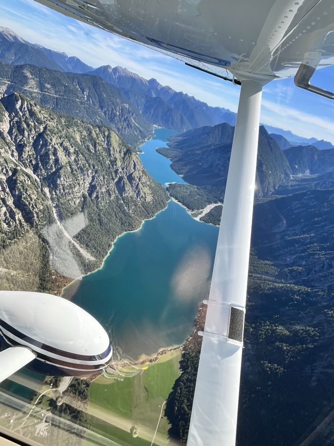 Blick aus der Cessna auf einen langgestreckten Bergsee zwischen bewaldeten Hängen
